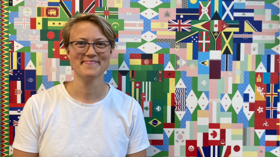 Malin. ny lärare för SPR1D, står framför en vägg prydd av en tapet med all världens flaggor.