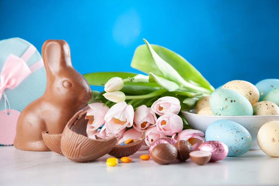En chokladkanin sitter bredvid några färgglada ägg.